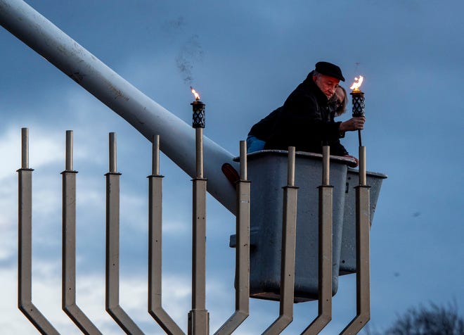 Herb Ginsburg places the candle Sunday for the first night of Hanukkah in the large menorah in Worcester's Newton Square. while John Young operates the bucket truck to reach the menorah.