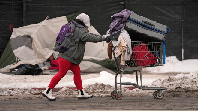 A woman pushes a cart past a tent along the sidewalk on Dec. 20, 2022, in Salt Lake City. Salt Lake City will make additional shelter beds available for people experiencing homelessness after five died in recent days amid subfreezing temperatures that are expected to plunge further throughout the United States this weekend.