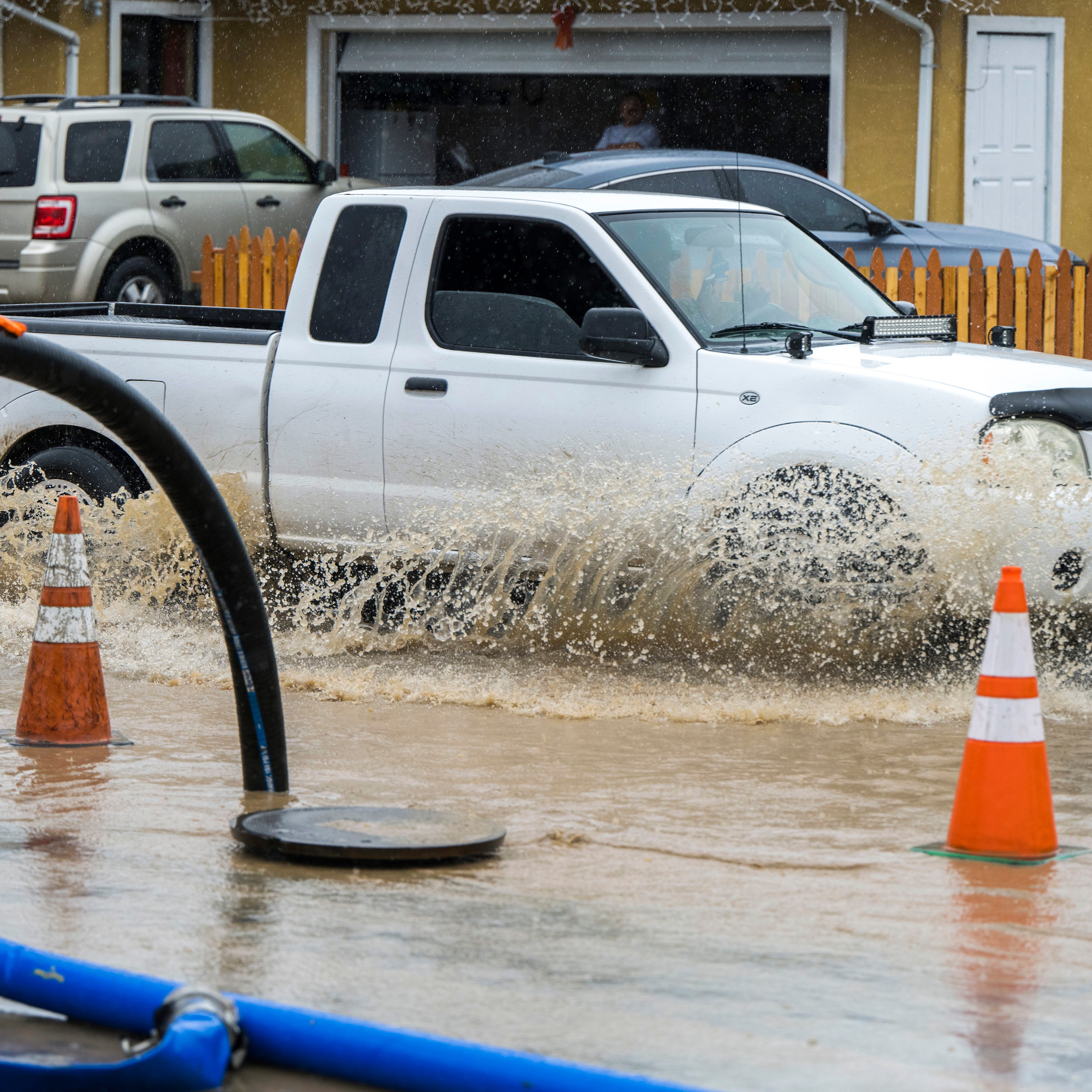 A member of public works clears a flooded storm drain on E Bolivar Street in Salinas, Calif., Tuesday, Dec. 27, 2022. The first in a week of storms brought gusty winds, rain and snow to California on Tuesday, starting in the north and spreading southward.  (AP Photo/Nic Coury)