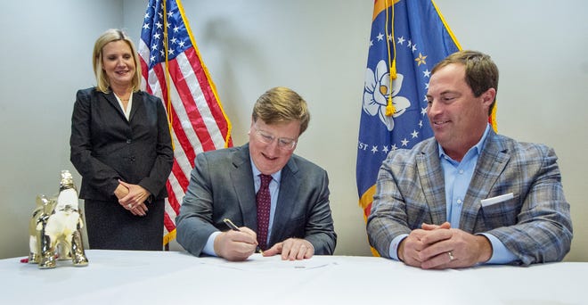 Gov. Tate Reeves, center, signs the Republican Candidate Party Nomination form to officially state his intent and qualifications to run for a second term as governor at the Mississippi Republican Headquarters in Jackson on Tuesday. With him is his wife Elee Reeves, left, and Mississippi Republican Party Chairman Frank Bordeaux, right.