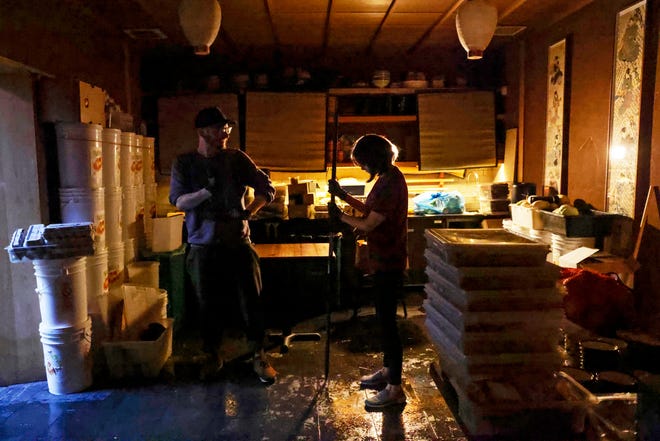 From left, Rintaro employees Aaron Linenberger and Akiko Mochizuki clean up from Saturday's floodwater at the restaurant on New Year's Day in San Francisco, Sunday, Jan. 1, 2023.
