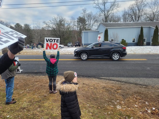 A person holds a "Vote No" sign above their head Saturday while another lifts a placard with the same message aloft from the sunroof of their car while exiting Hardwick Elementary School, where voting took place on whether to allow a proposed horse racing track to move forward in town.