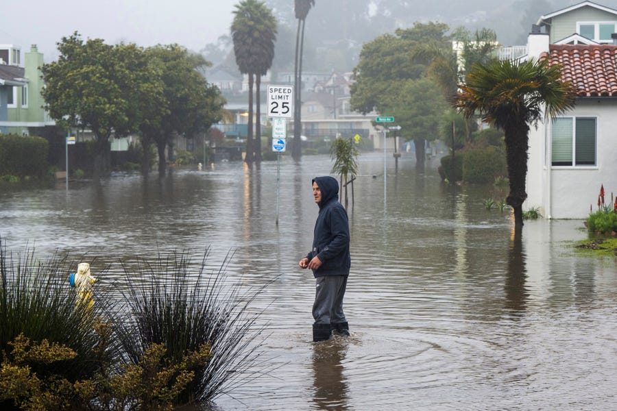A man wades through a flooded street in the Rio Del Mar neighborhood of Aptos, Calif., Monday, Jan. 9, 2023.