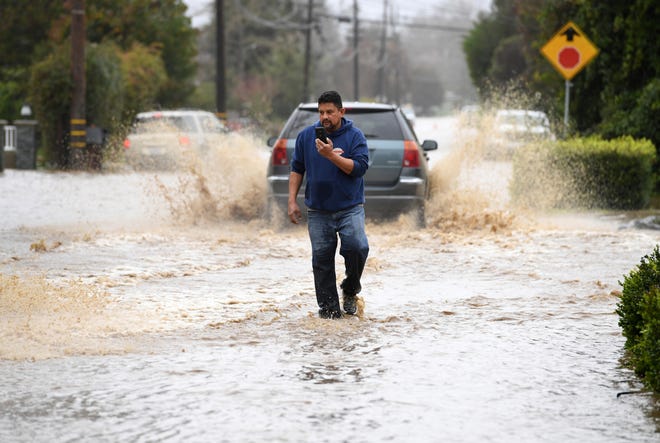 Residents walk along College Road after it was flooded in recent storms in Watsonville, Calif., Monday, Jan. 9, 2023.