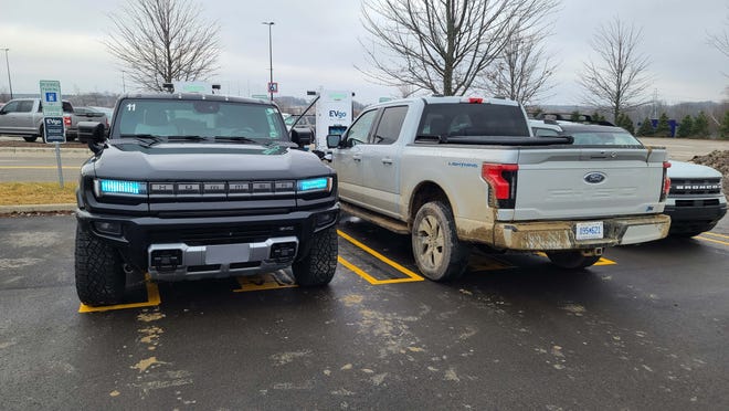 The 2023 Ford F-150 Lightning EV charges at EVgo Great Lakes Crossing next to a GMC Hummer EV.