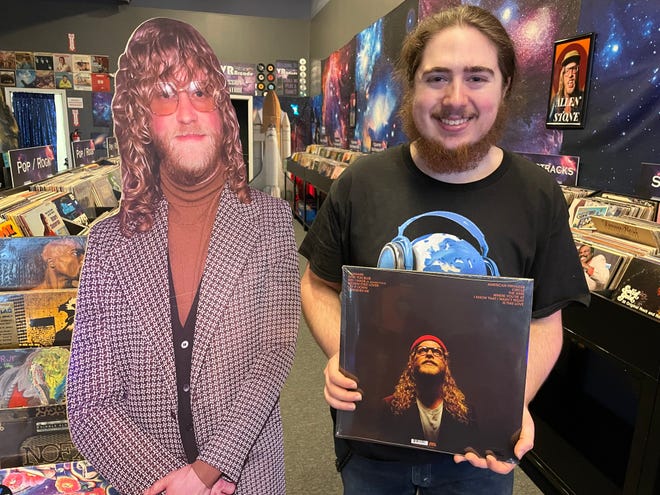 Galaxy Records owner Aidyn Messerschmidt stands next to a cardboard cutout of musician Allen Stone while holding one of his albums at the new store in Genoa Township, shown Thursday, Jan. 12, 2023.