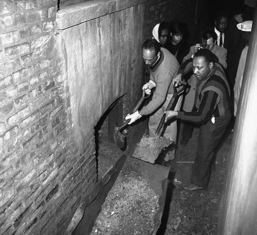 Martin Luther King attacks slum conditions at an apartment building in Chicago, Illinois on Feb. 23, 1966 where R.V. Towns lives with his wife Risoe and seven children. Al Raby, CCO, and King and several Catholic priests use shovels to clean up wheelbarrows of trash and ashes from the basement from stair steps.