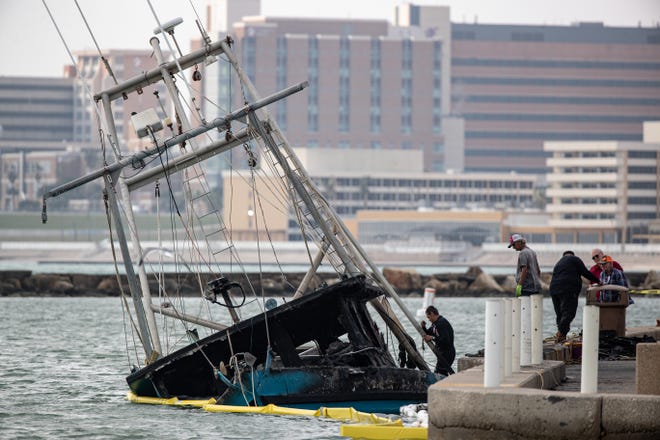 A burned shrimp boat floats in the marina near Coopers Alley L-Head on Monday, Jan. 16, 2023, in Corpus Christi, Texas. The boat caught fire on Sunday releasing oil and fuel into the water. Booms surround the boat to contain the spill, according to a press release from the City.