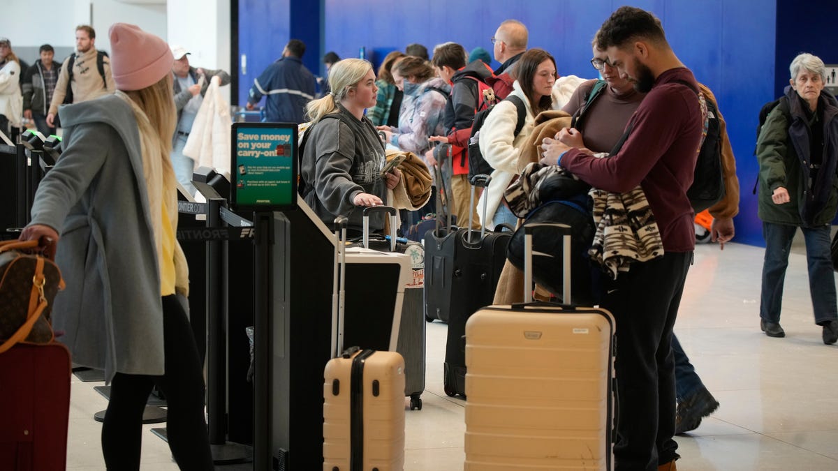 Travelers queue up at the check-in kiosks for Frontier Airlines in Denver International Airport Friday, Dec. 30, 2022, in Denver. (AP Photo/David Zalubowski)