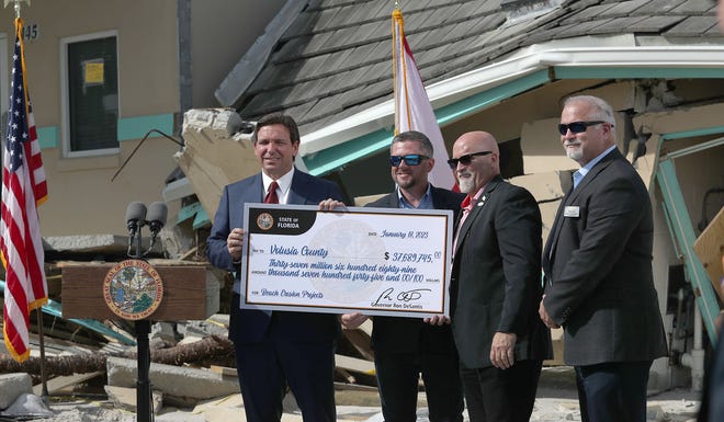 Gov. Ron DeSantis hands a check to, from left, Volusia County councilmen Danny Robins and Matt Reinhart and County Manager George Recktenwald on Wednesday, Jan. 18, 2023, on the beach ramp at Dunlawton and Atlantic avenues in Daytona Beach Shores. DeSantis has earmarked another $37.6 million for Volusia County for beach erosion following tropical storms Ian and Nicole.