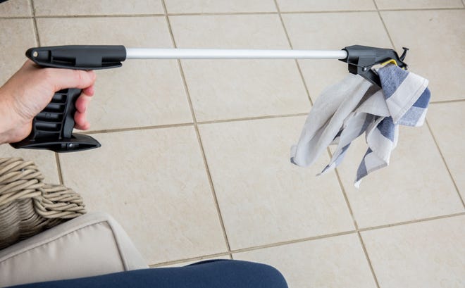 A person uses a reacher-grabber to pick up a towel.
