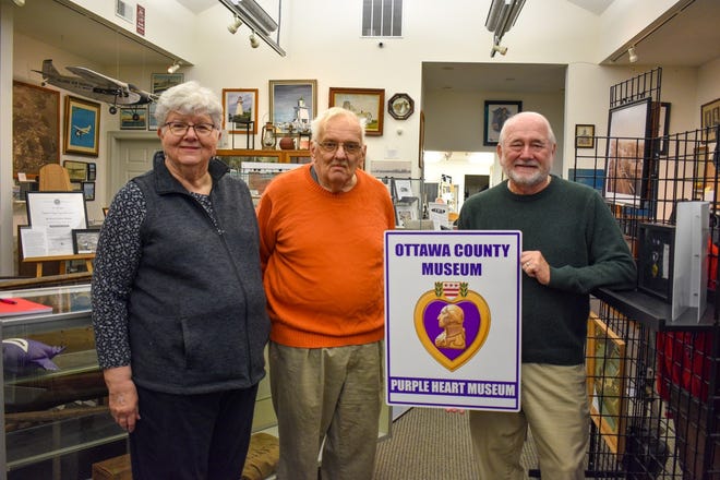 Ottawa County Museum Curator Peggy Debien, Area Heritage Foundation President James Rusincovitch and Museum Board Member David Barth display the Purple Heart Museum sign that will be displayed outside the building. The museum was designated a Purple Heart Museum thanks to the efforts of Barth.