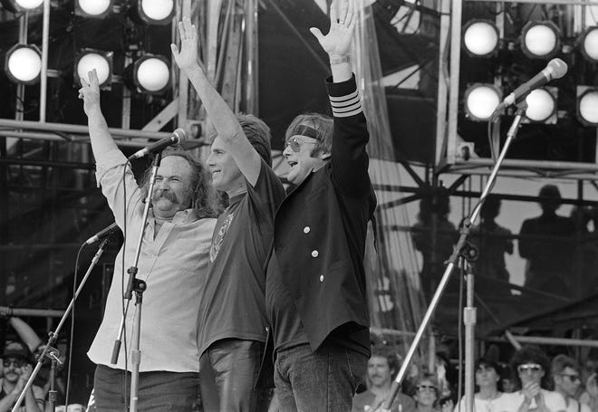 David Crosby, Graham Nash e Stephen Stills acenam para a multidão durante sua apresentação no Live Aid no JFK Stadium, na Filadélfia, em 13 de julho de 1985.