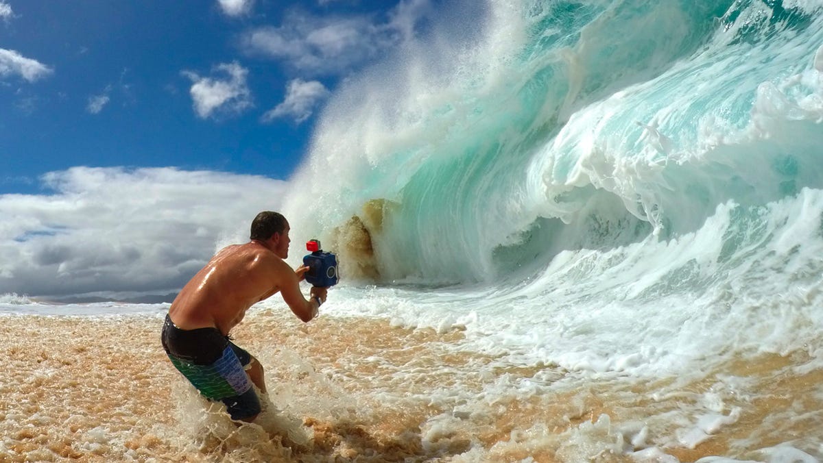 Clark standing in shallow water capturing a powerful shorebreak wave on the North Shore of Oahu.