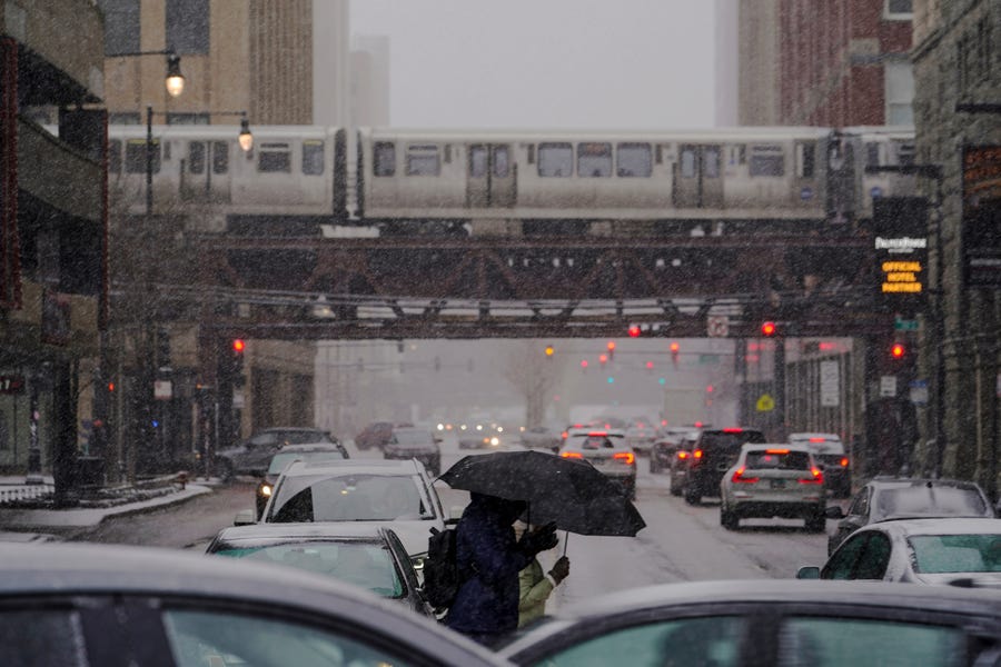 People walk in the snow as Chicago's famed L train moves along Saturday, Jan. 28, 2023, in downtown Chicago.