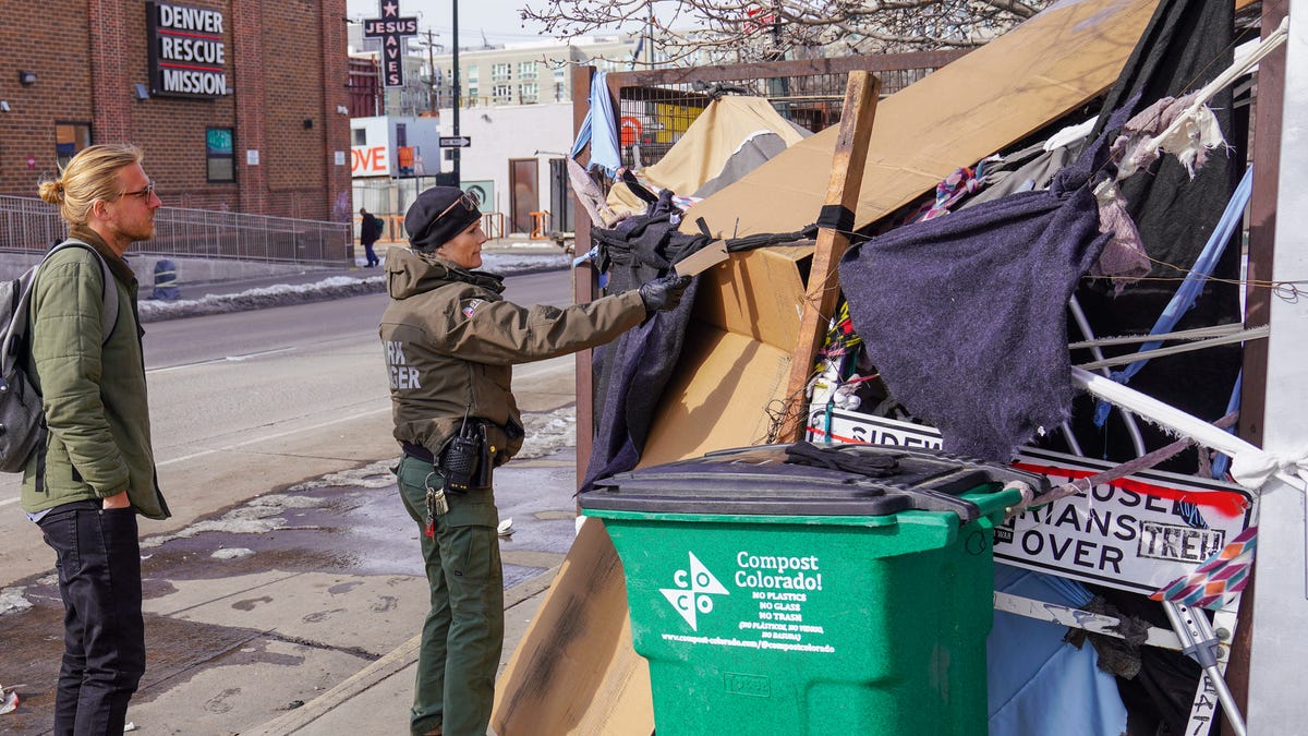 Denver park ranger Jodie Marozas looks into a pile of belongings in a city park in Denver as Tom Kaiser, a mental health clinician with WellPower, looks for the owner. Across the country, officials are clearing away more tent encampments.
