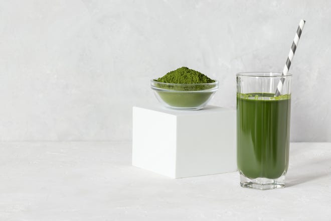 Green drink in a glass and powder on a white concrete background.