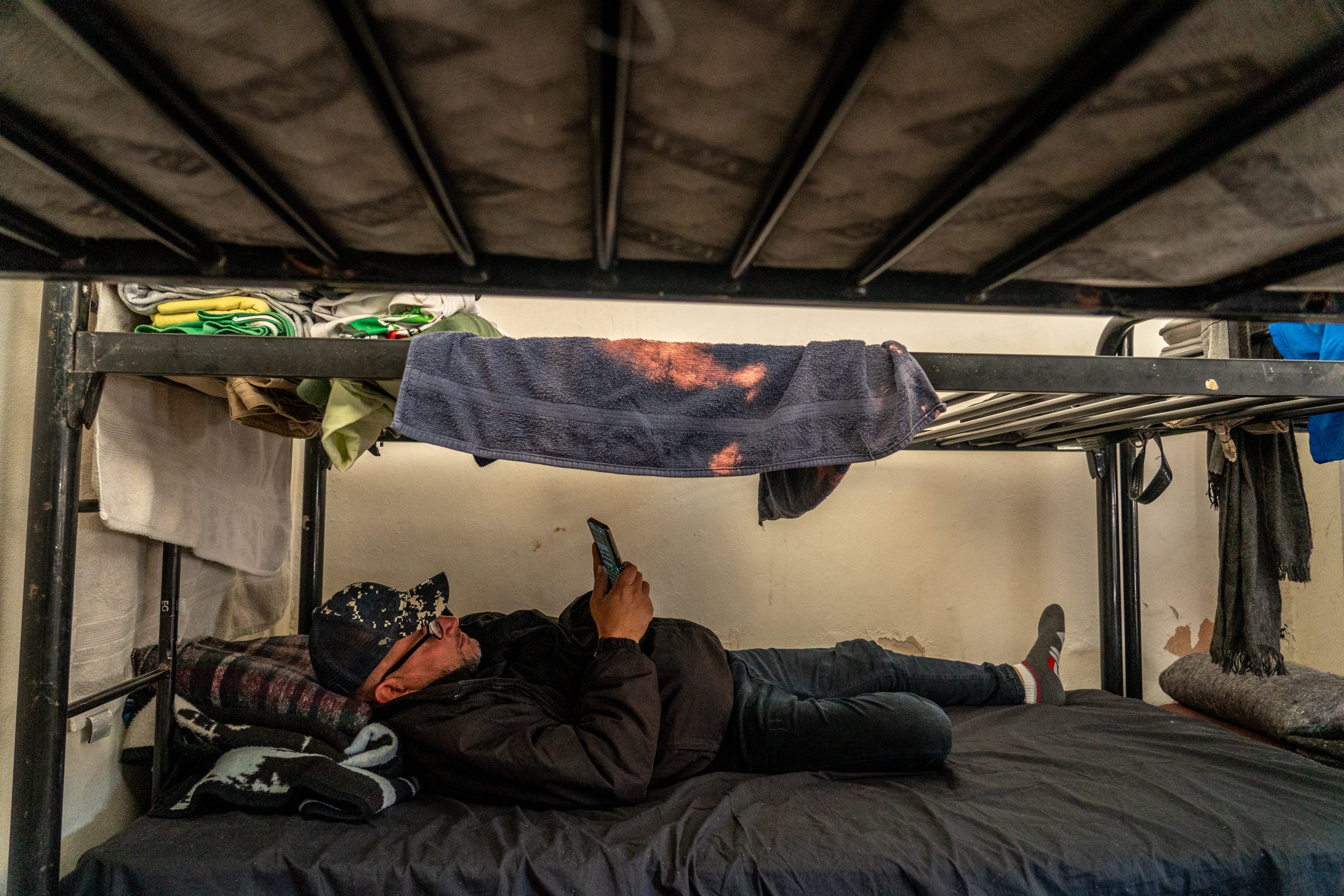 Yorjel Navarro, de 42 años, de Cuba, envía mensajes a familiares y amigos mientras está acostado en una cama dentro de las viviendas en la Casa del Migrante la Divina Providencia, un albergue para migrantes, en San Luis Río Colorado, Sonora, México, el 2 de febrero. 2023.