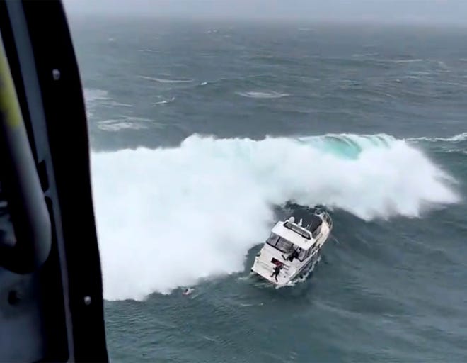In this photo provided by the U.S. Coast Guard Pacific Northwest, a Coast Guard rescue swimmer reaches a boat right before a giant wave rolled the craft at the mouth of the Columbia River in Oregon on Feb. 3. The newly minted Coast Guard rescue swimmer saved the life of a man who was piloting the yacht. (AET1 Kyle Turcotte/U.S Coast Guard Pacific Northwest via AP)