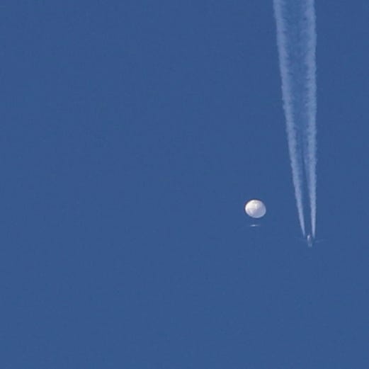 In this photo provided by Brian Branch, a large balloon drifts above the Kingstown, N.C. area, with an airplane and its contrail seen below it. The United States says it is a Chinese spy balloon moving east over America at an altitude of about 60,000 feet (18,600 meters), but China insists the balloon is just an errant civilian airship used mainly for meteorological research that went off course due to winds and has only limited 