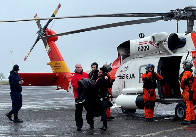 In this photo provided by the U.S Coast Guard Pacific Northwest, Coast Guard personnel help carry a swimmer from a rescue helicopter after he was rescued from the mouth of the Columbia River after his boat was capsized by a giant wave on Friday, Feb. 3, 2023, at Coast Guard Base Astoria, Ore.