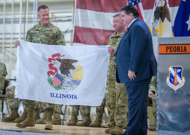 Major General Richard R. Neely, Commander of the Illinois National Guard, left, and Lt. Col. Jason Celletti, commander of the 1st Assault Helicopter Battalion, 106th Aviation Regiment, middle, present an Illinois flag to Gov. JB Pritzker during a mobilization ceremony for the regiment Tuesday, Feb. 7, 2023 at the 182nd Airlift Wing in Peoria.