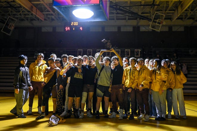 The Holt wrestling team celebrates with the district championship trophy after the Rams' victory over Grand Ledge on Wednesday, Feb. 8, 2023, in Holt.