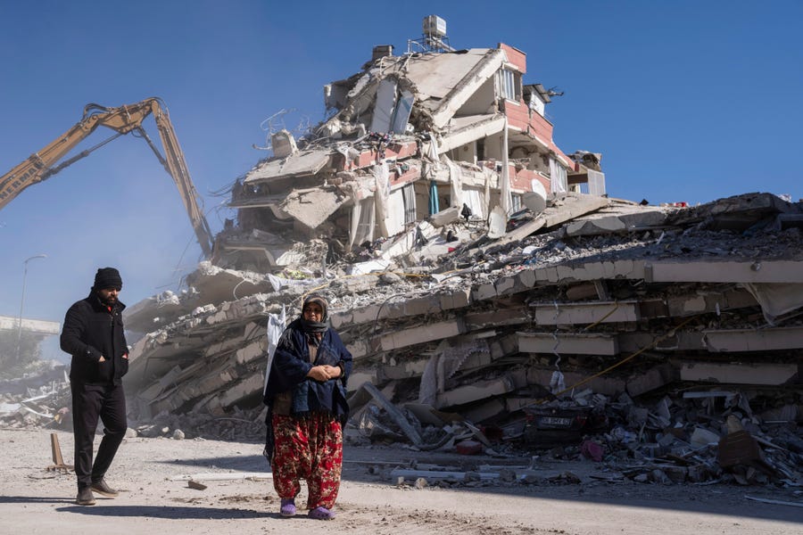 Local residents walk in front of a destroyed building in Nurdagi, southeastern Turkey, Thursday, Feb. 9, 2023. Thousands who lost their homes in a catastrophic earthquake huddled around campfires and clamored for food and water in the bitter cold, three days after the temblor and series of aftershocks hit Turkey and Syria.