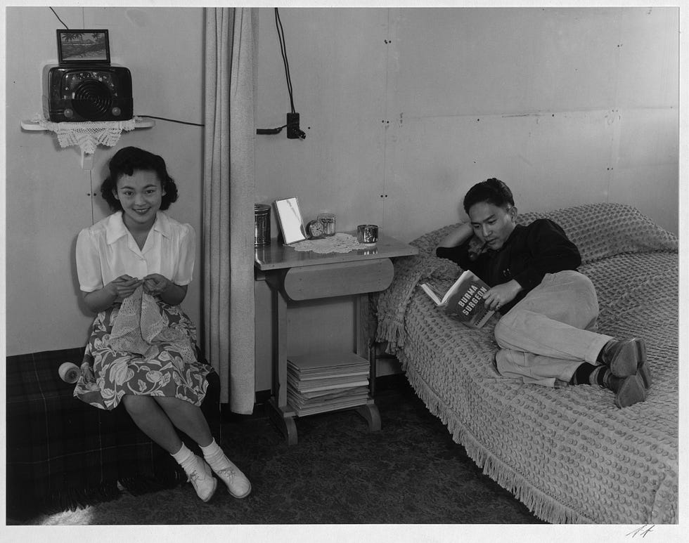 Japanese incarceration in the United States in Adams’ photos 22 Shimizu sitting on a couch with lace, and Mr. Shimizu lying on a bed, reading.
