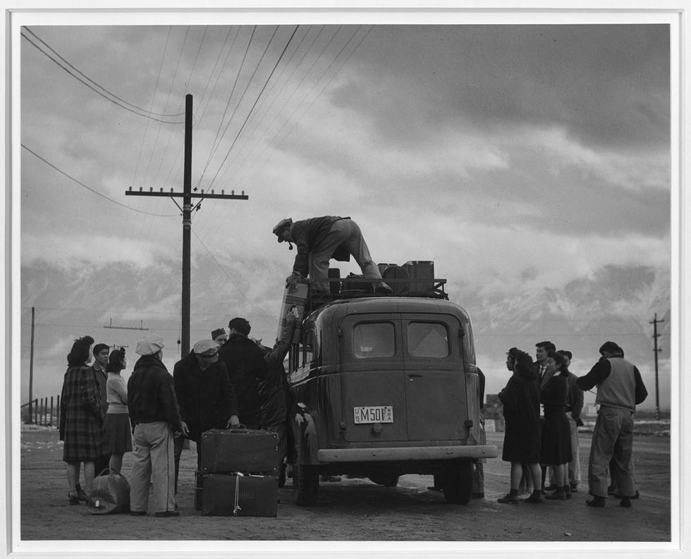 Japanese incarceration in the United States in Adams’ photos 6 A man stands over a bus loading luggage into a rack as people are herded around a bus and forcibly transferred to a burial camp.