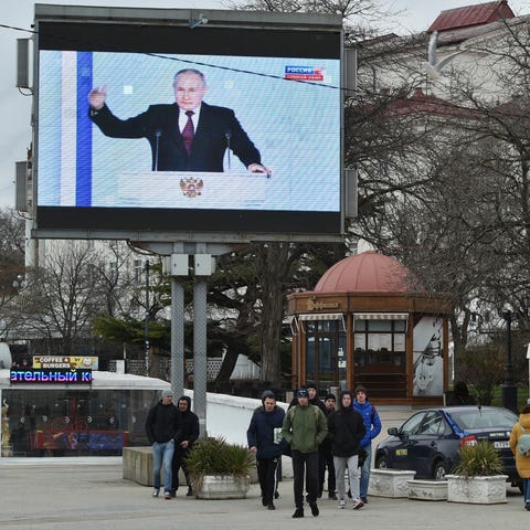 People walk in front of a tv screen showing Russia