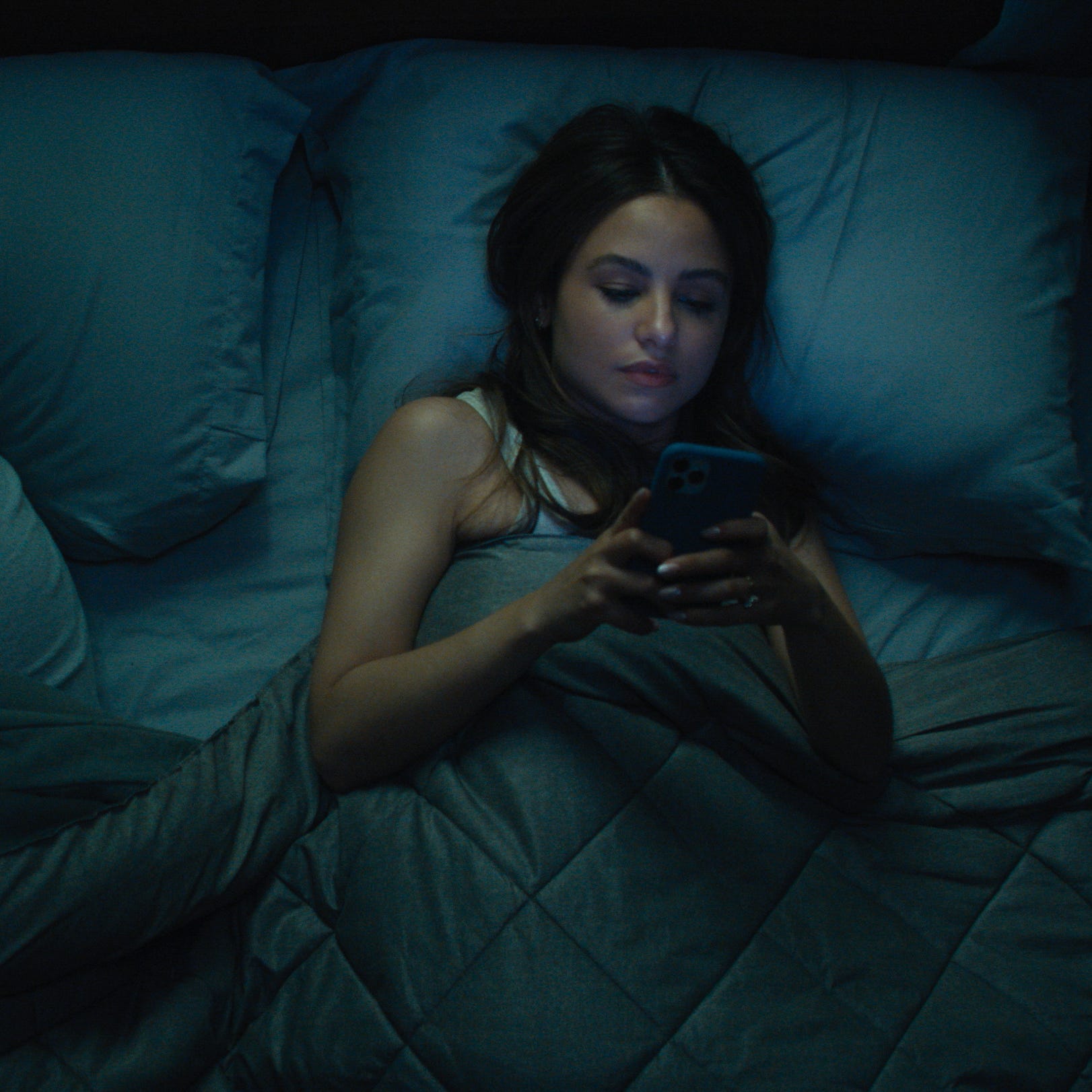 As Craig (Nat Wolff) sleeps, his fiancée Patti (right, Aimee Carrero) answers a late night text from Regus Patoff, the odd new boss at Craig's company.