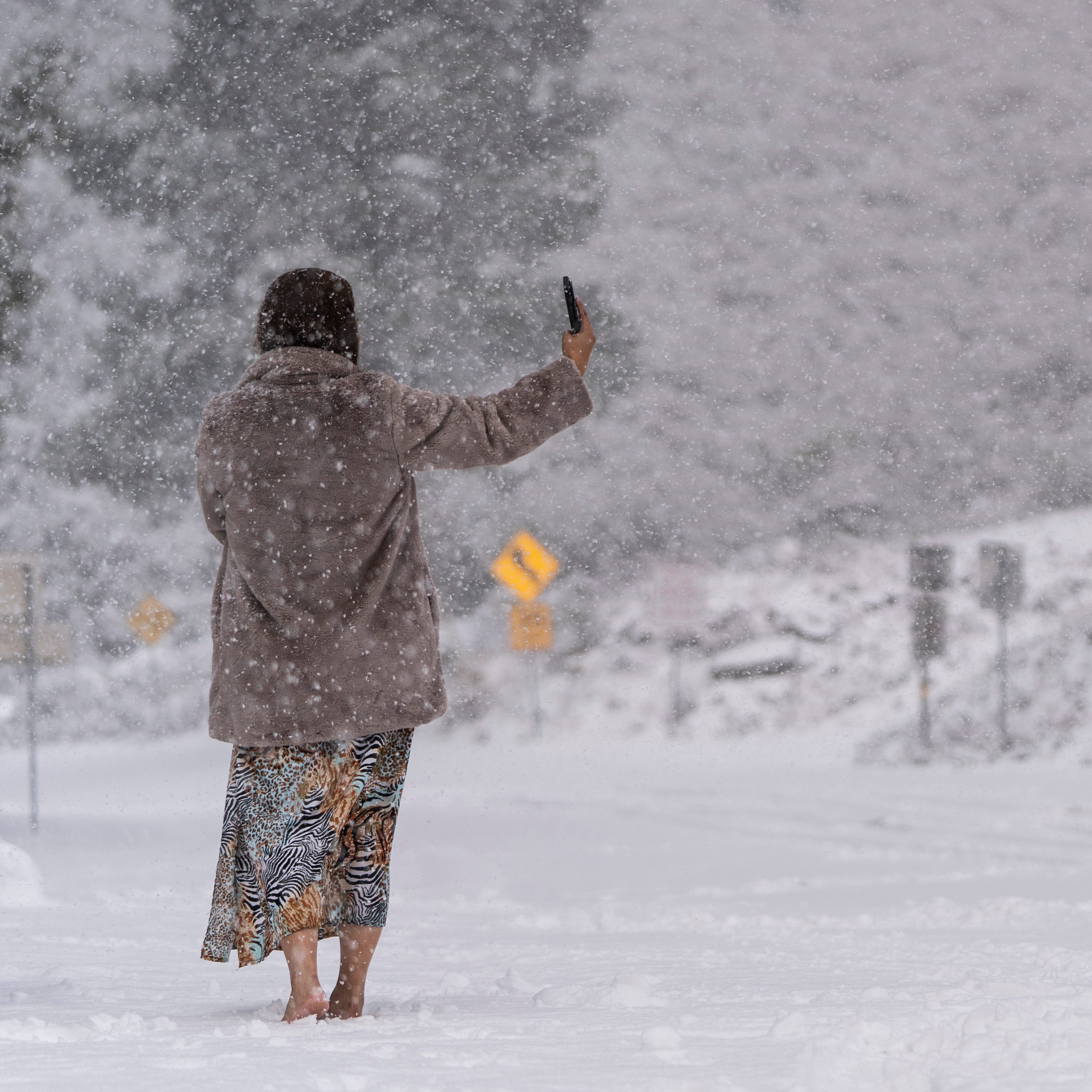 A visitor stands on a snow-covered road while taking a selfie in the Angeles National Forest near La Canada Flintridge, Calif., Thursday, Feb. 23, 2023.