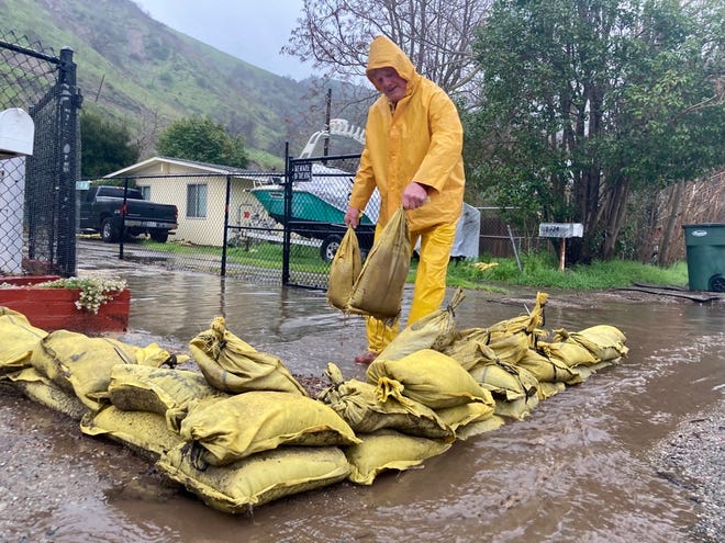 John O'Connor places sandbags on Nye Road near Casitas Springs as rain moves through Ventura County Friday morning, Feb. 24, 2023.  O'Connor said she was carrying sandbags outside to get her daughter coffee.