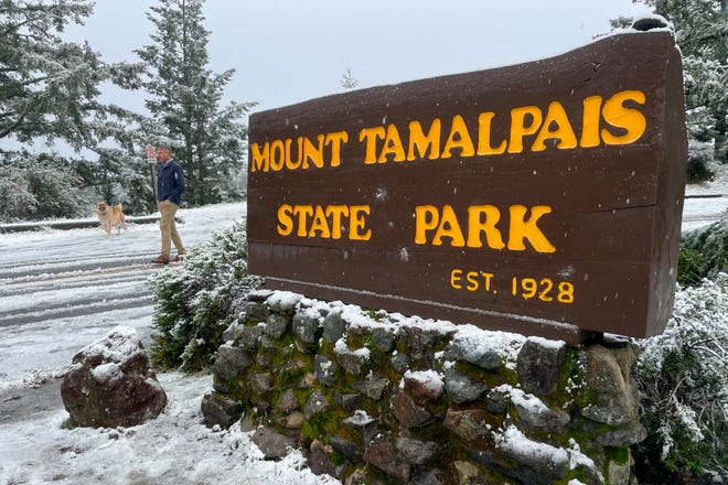 A man walks near the entrance to snow-covered Mount Tamalpais State Park in Mill Valley, Calif., Friday Feb. 24, 2023. California and other parts of the West are facing heavy snow and rain from the latest winter storm to pound the United States. The National Weather Service has issued blizzard warnings for the Sierra Nevada and Southern California mountains.