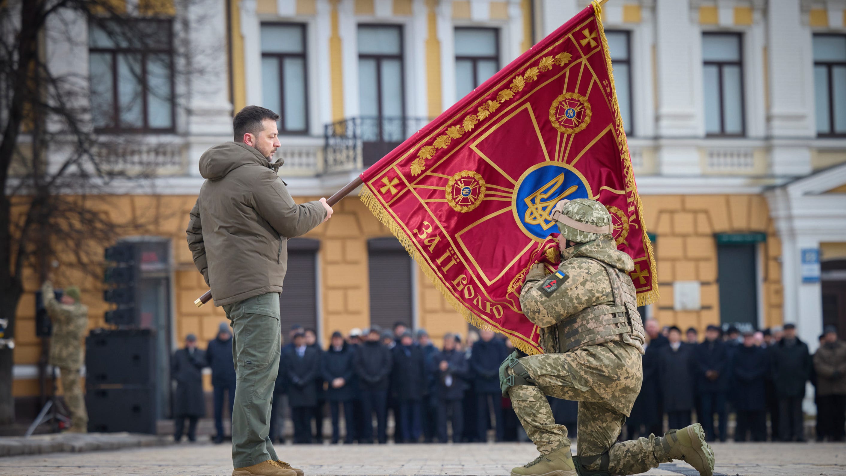 Ukrainian President Volodymyr Zelenskyy, left, holds the flag of a military unit as an officer kisses it, during commemorative event on the occasion of the Russia Ukraine war one year anniversary in Kyiv, Ukraine, Friday, Feb. 24, 2023.