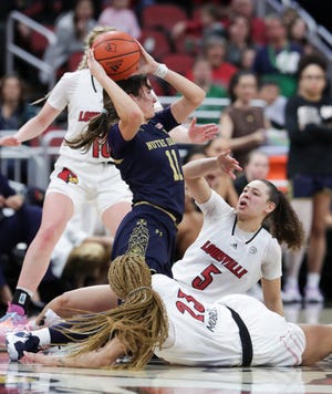 Notre Dame's Sonia Citron (11) tried to get rid of the ball as she hit the deck against the defense of U of L's  Mykasa Robinson (5) and Alexia Mobley (23) during their game at the Yum Center in Louisville, Ky. on Feb. 26, 2023.