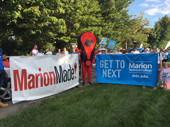The MarionMade! mascot, Mark, stands proudly between the MarionMade! banner and the Marion Technical College banner before the start of the Popcorn Festival Parade in September 2019.