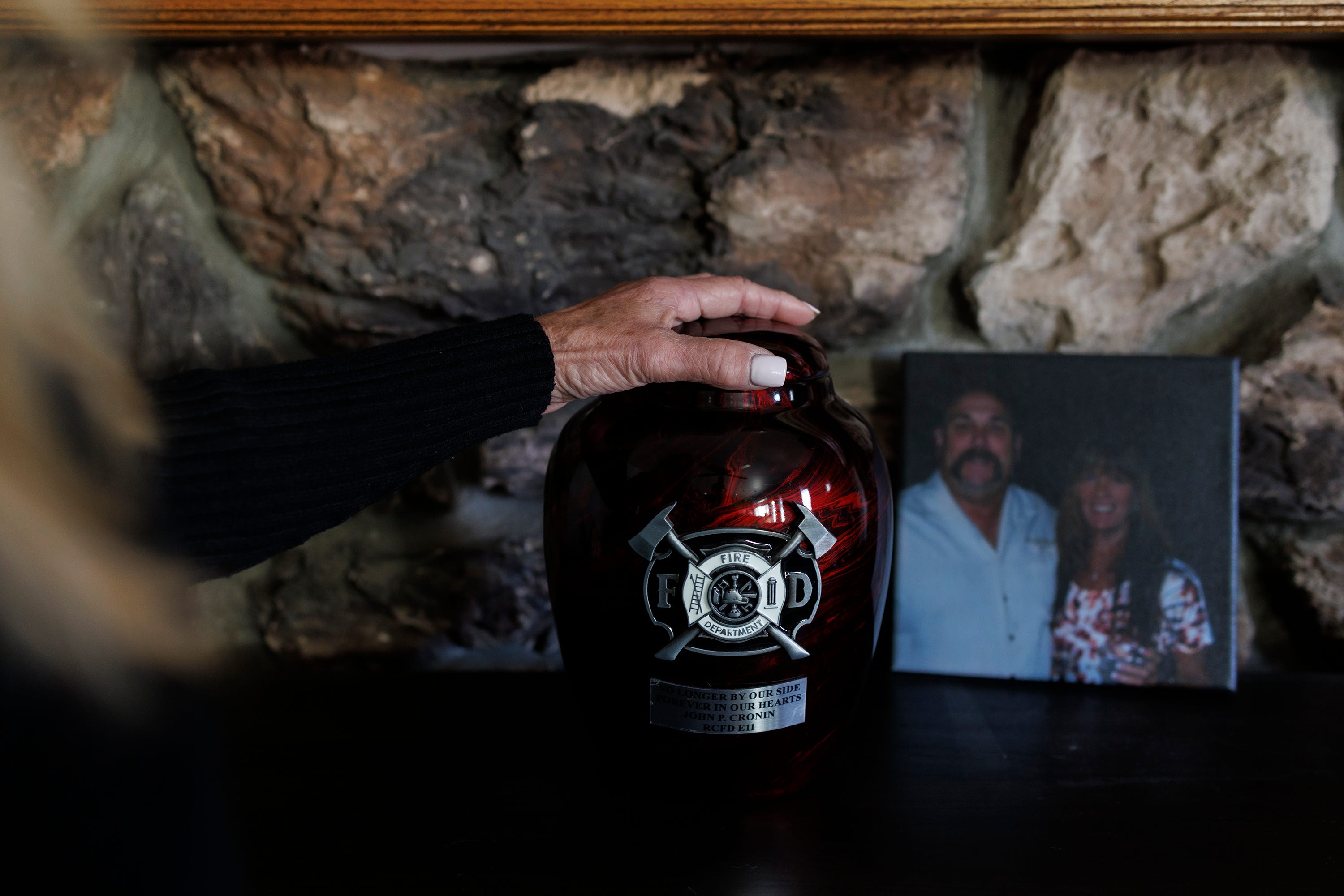 Jocelyn Cronin puts her hand on her husband's urn at the altar she made in his memory in her home in Petaluma, California.