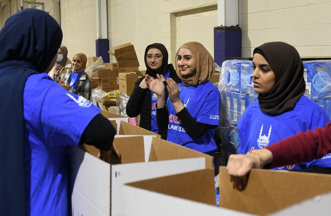 Volunteers Sarah Khan, left, 18, Jasmine Khan, 20, and Ehsanne Saleh, 18, all of Dearborn, pause for a moment and Jasmine claps as another pallet of food boxes is complete as volunteers pack up boxes of food for the Islamic Relief USA.