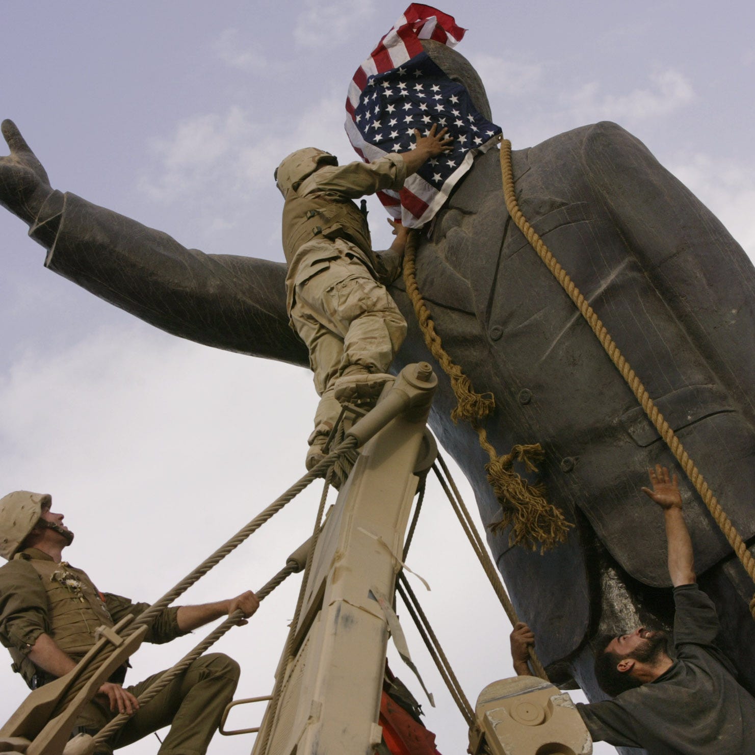 In this file photo taken Wednesday, April 9, 2003, an Iraqi man, bottom right, watches Cpl. Edward Chin of the 3rd Battalion, 4th Marines Regiment, cover the face of a statue of Saddam Hussein with an American flag before toppling the statue in downtown in Baghdad, Iraq.