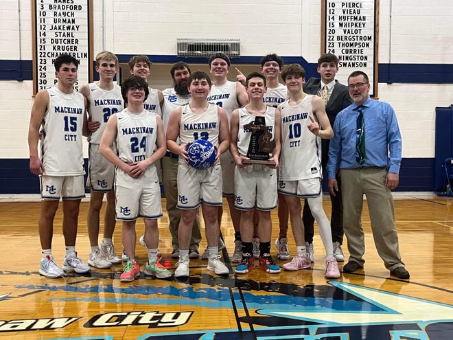 The Mackinaw City boys basketball team holds up the district title trophy after beating Harbor Light at home on Friday.