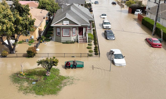 An aerial view shows people sitting on a bench in a flooded neighborhood in the unincorporated community of Pajaro in Watsonville, California on March 11, 2023.