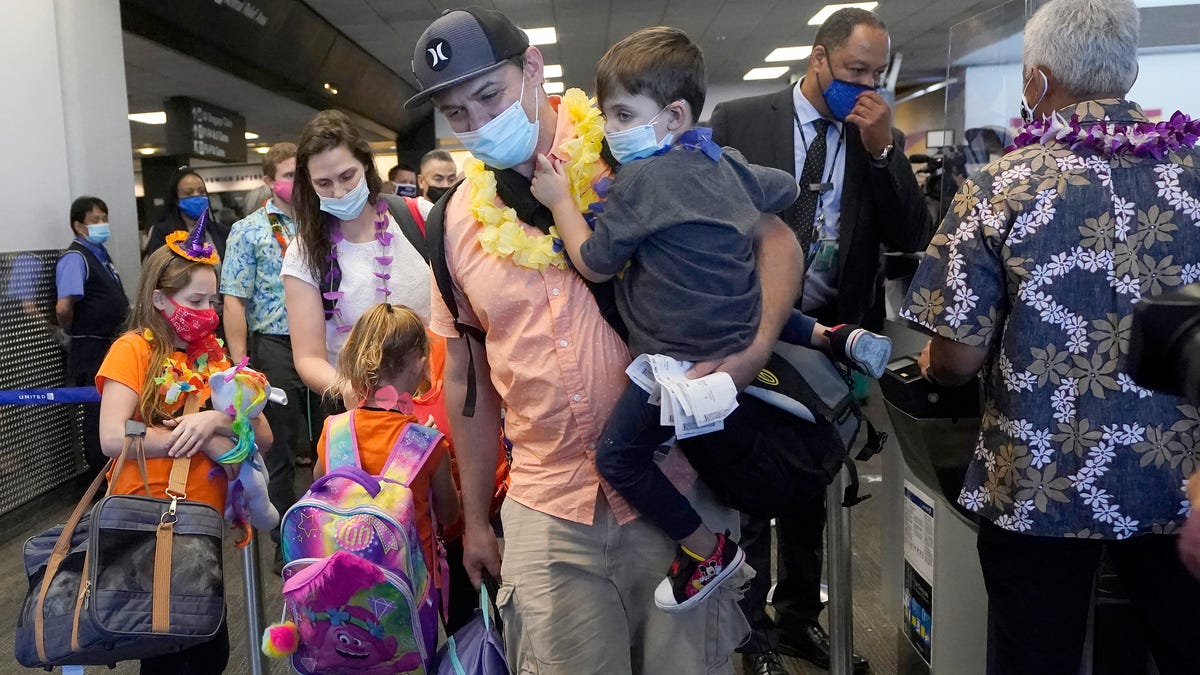 In this Oct. 15, 2020 file photo, Hawaii resident Ryan Sidlow carries his son Maxwell as their family boards a United Airlines flight to Hawaii at San Francisco International Airport. (AP Photo/Jeff Chiu, File)