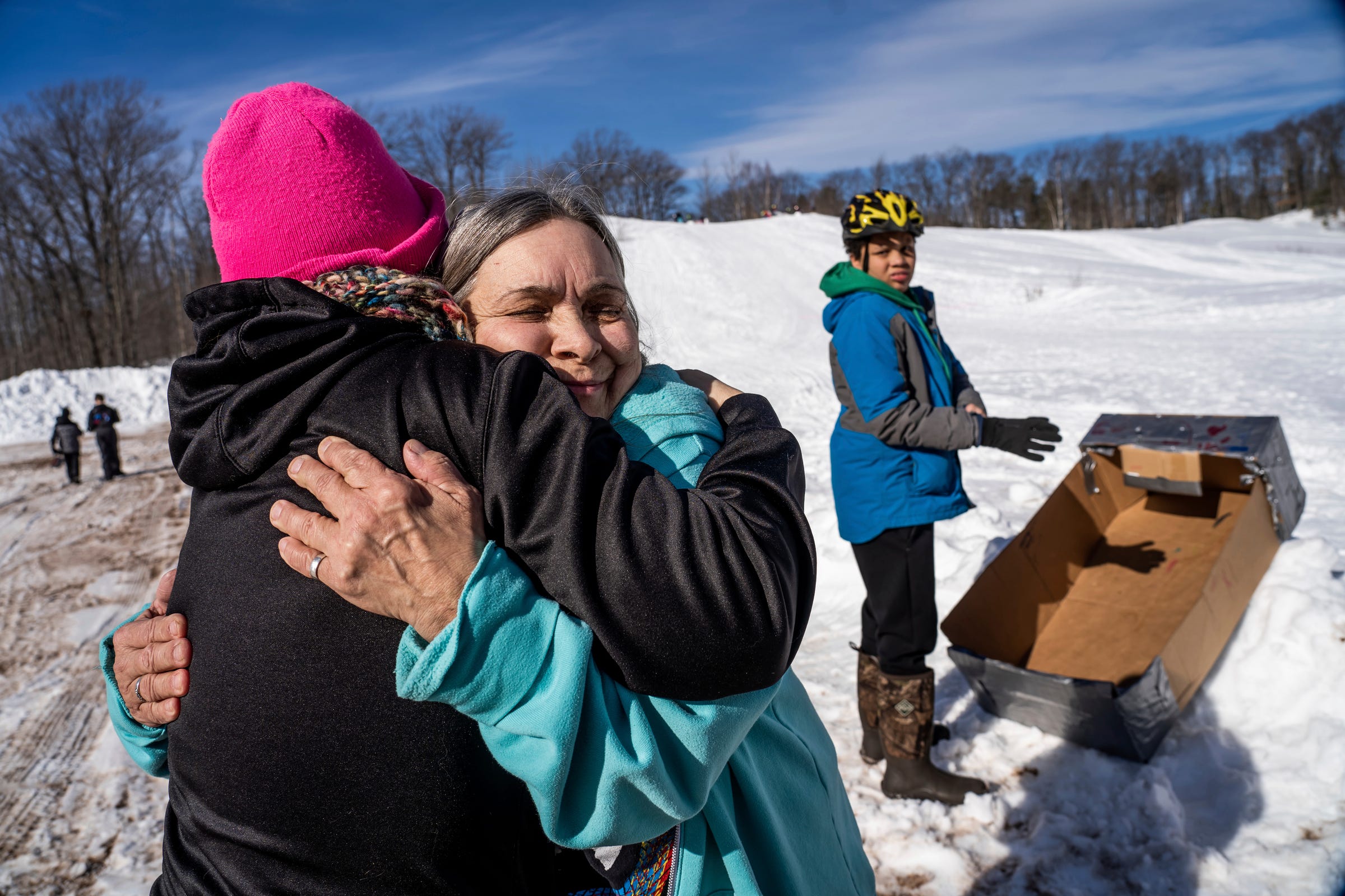 Geriann Bialkowski, center, hugs Denise Venturato as they waited for the start of the K.I. Sawyer Cardboard Sled Races on Feb. 11, 2023.
