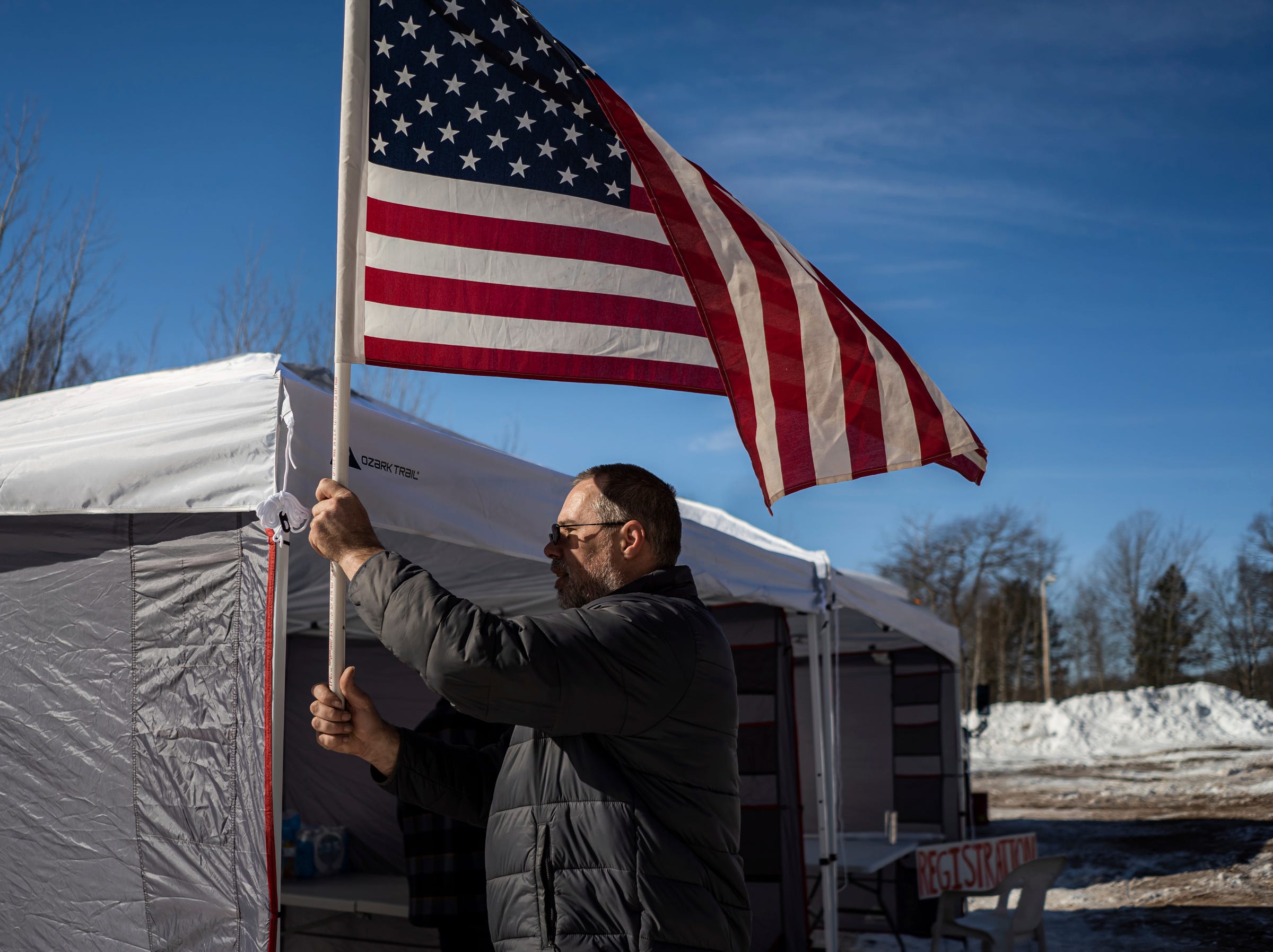 Ryan Lipinski moves to tie an American flag to a tent pole before the start of the annual K.I. Sawyer Cardboard Sled Races on Feb. 11, 2023. The disabled veteran organized the event to give kids on the former Air Force base something to do during the long U.P. winter.