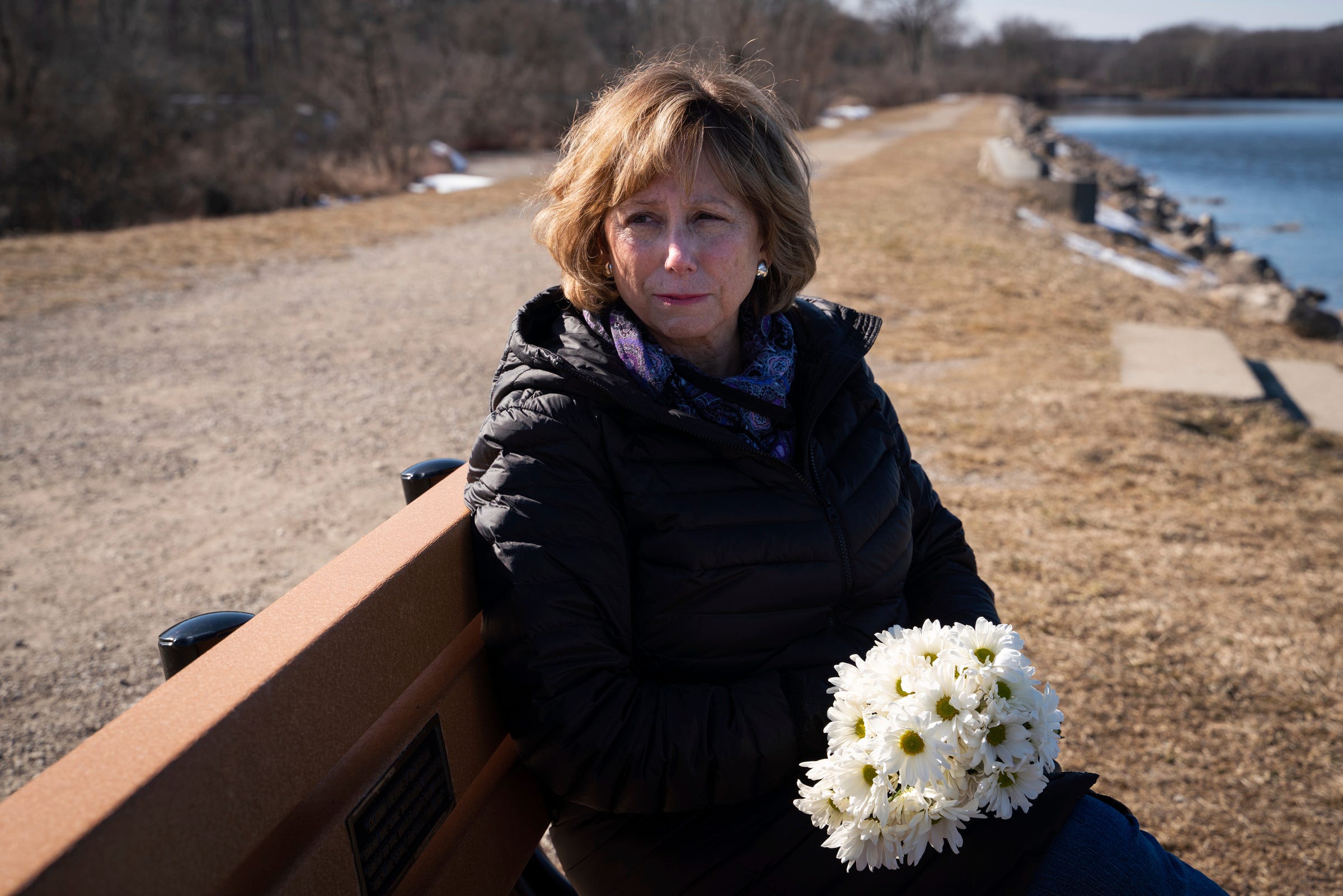 Mary Moffett sits at a bench made by family and friends to honor her daughter, Quinn Moffett in Ann Arbor on Wednesday, March 16, 2023. The bench is located near the water in a spot that Quinn, 21, frequently visited with her friends while in high school.