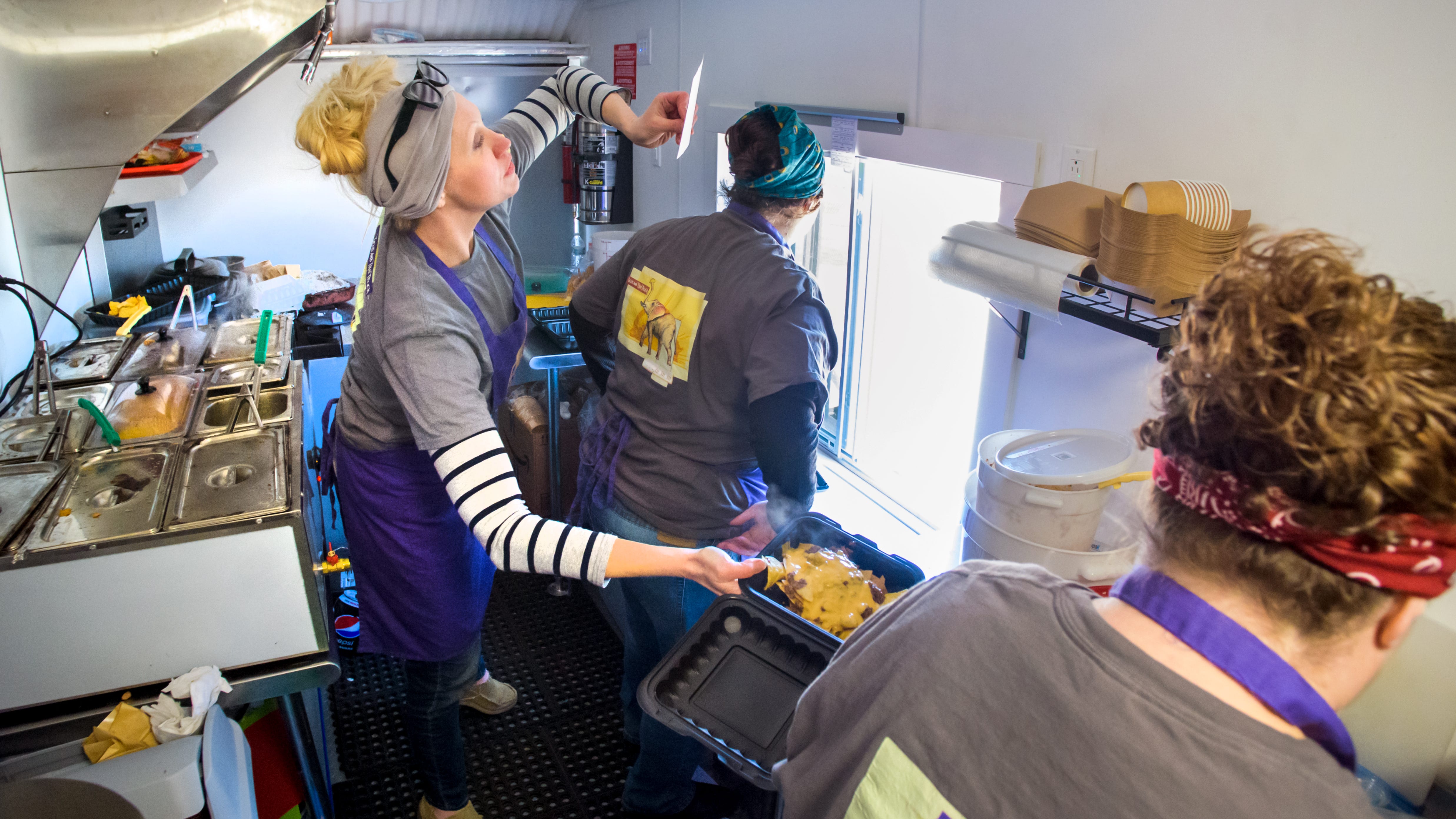Laura Lytle checks a ticket while handing over an order of nachos to business partner and food prepper Devin Wyman as Kat Ashdown serves customers at the window of the Tacos and Thai food truck during a visit to Illinois CancerCare off Route 91 in North Peoria.