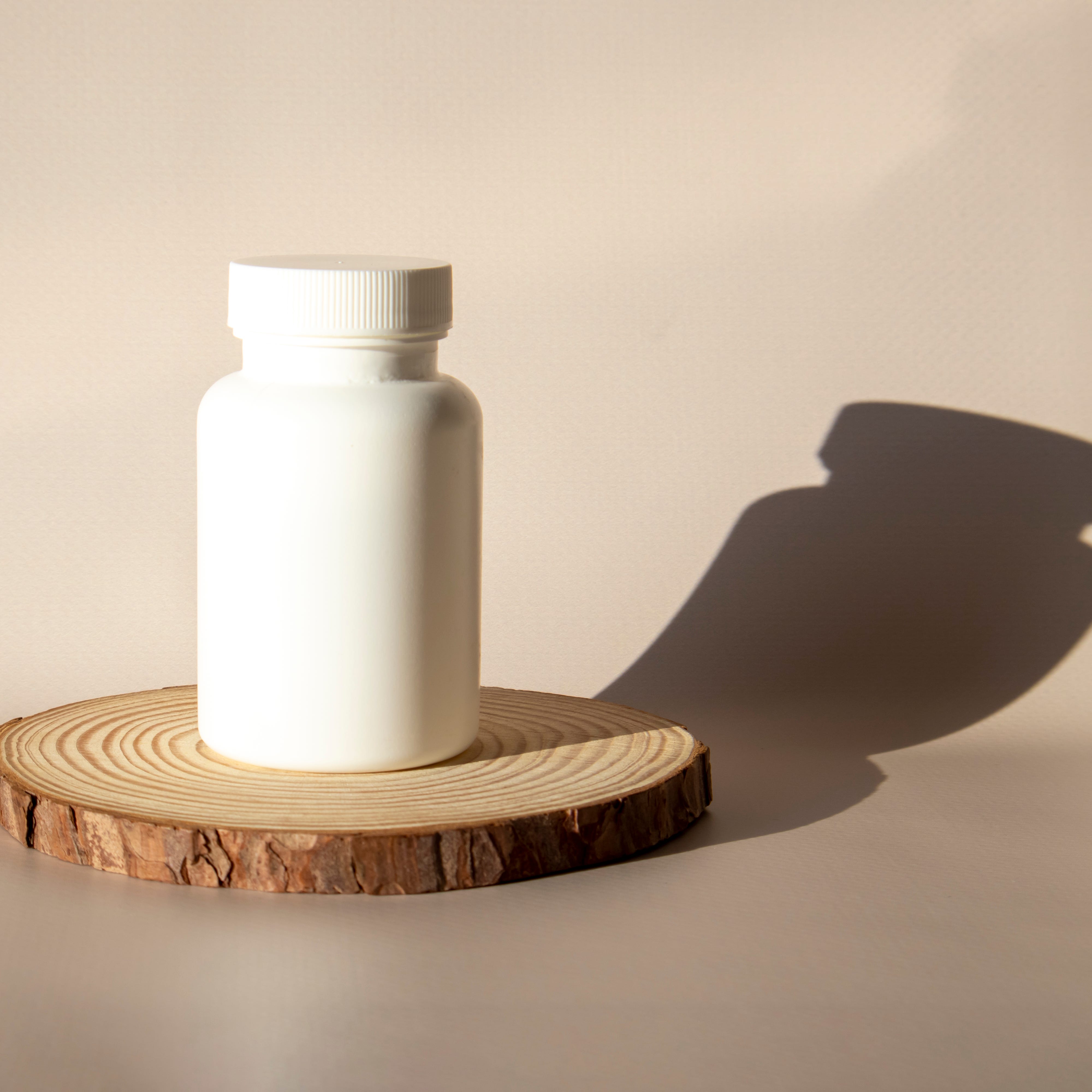 Mock-up of a white pill and supplement big jar on a wood podium on a beige background in the sun