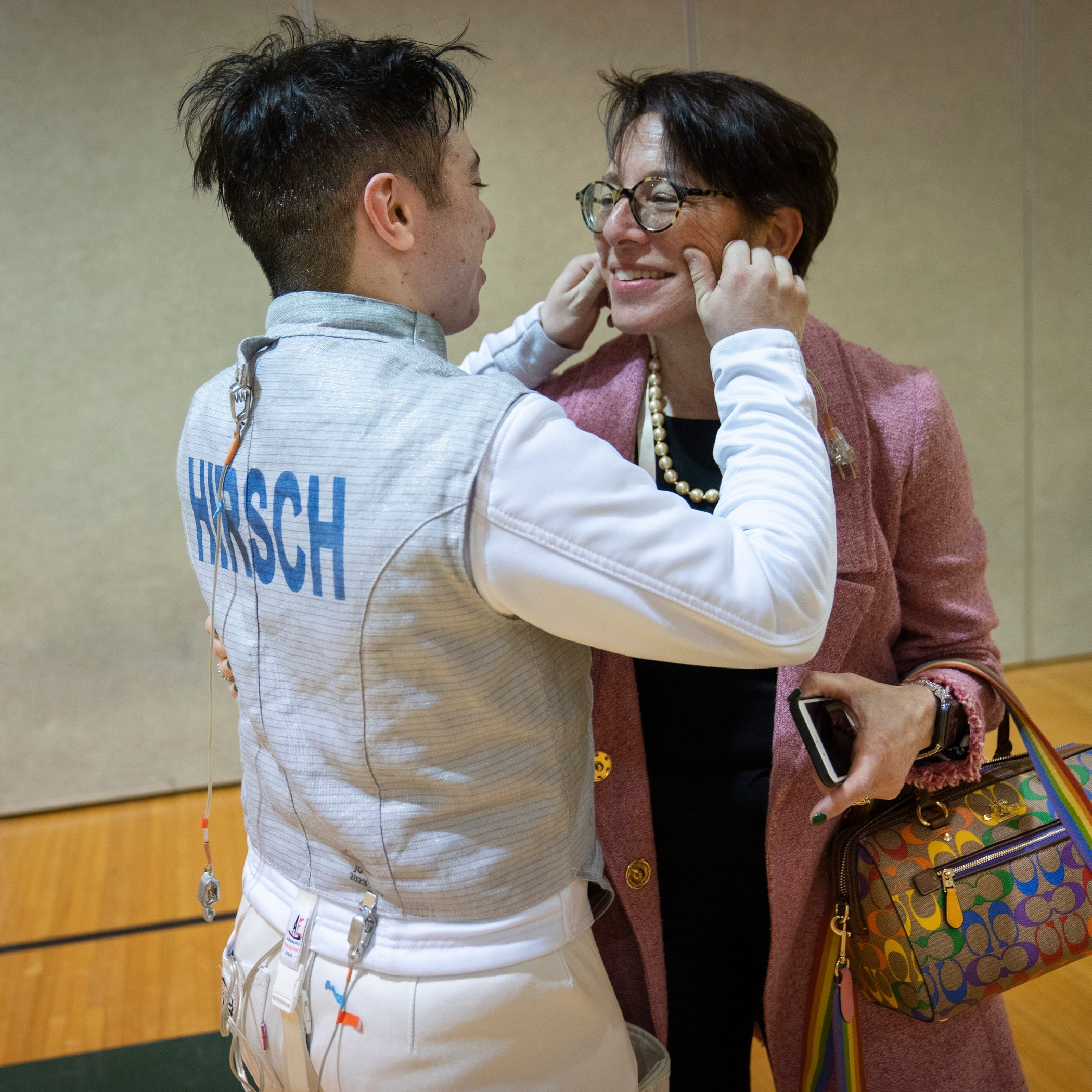 Bobbie Hirsch, 19, a biology major from Huntington Woods, left, pinches his mother, Lauren Hirsch's cheeks in between practices with his Wayne State fencing teammates Tuesday, March 21, 2023 in the Wayne State University Matthaei Center. Hirsch, a transgender man, joked about his mother's pride-themed Coach purse Òshe insisted on buying something that screamed ally as the two shared a laugh.